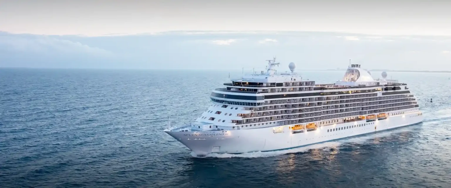 A world-cruise ship sailing past a coastal landmark
